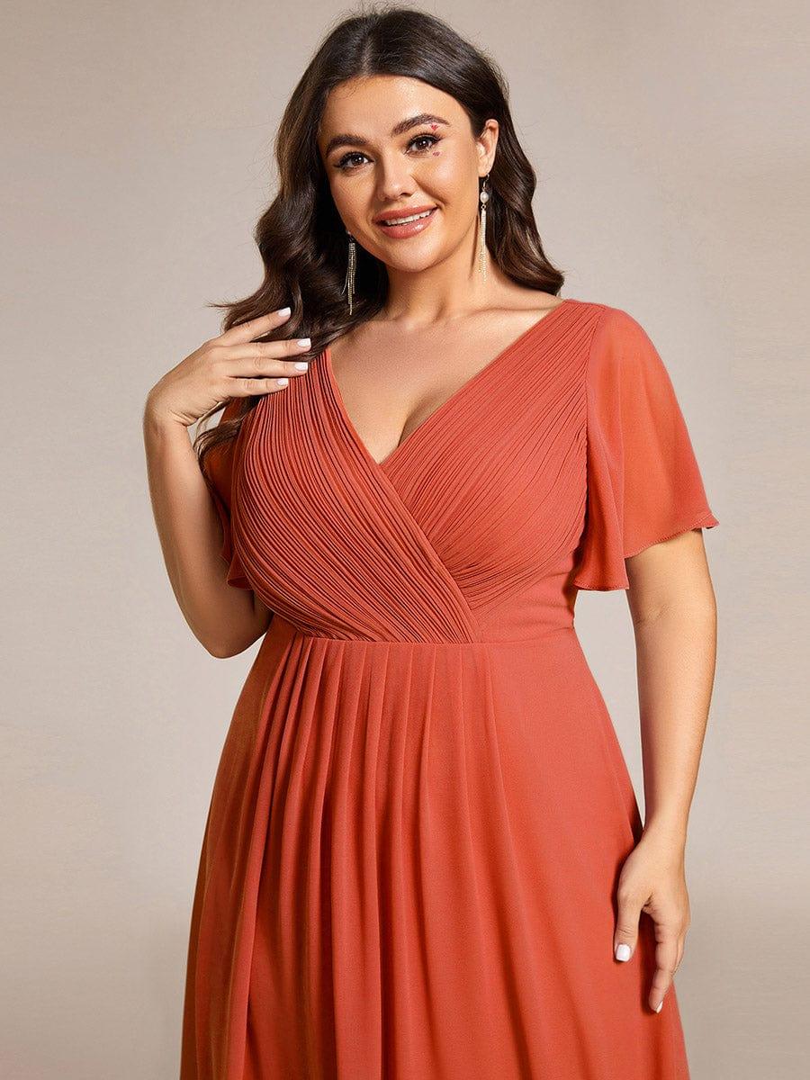 Close-up of the burnt orange dress's pleated V-neck bodice and flutter sleeve on a smiling plus-size model. 99