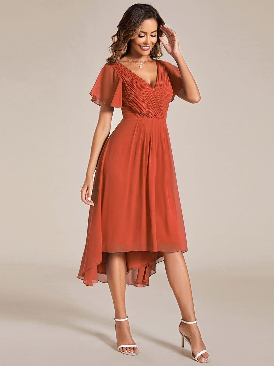 Burnt orange dress seen from a three-quarter angle, the model smiling with one hand raised to her hair. 96