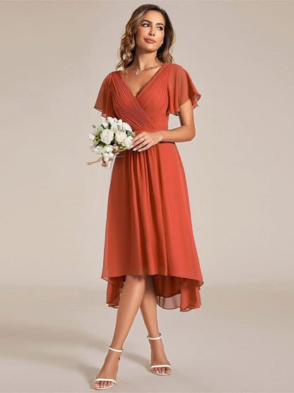 Model in the burnt orange dress holding a small bouquet of white flowers, looking to the side. 95