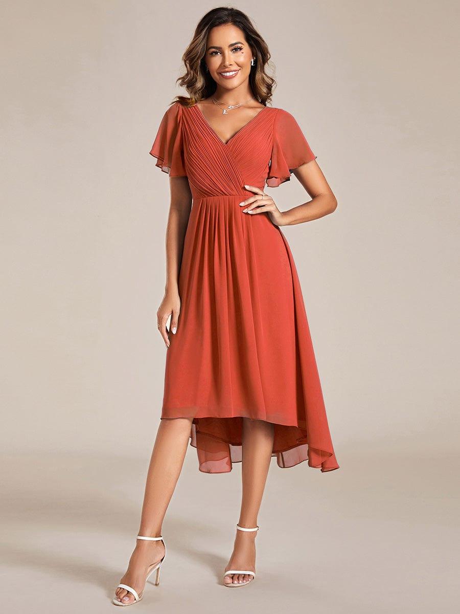 Model in the burnt orange chiffon dress, front view, hand on hip, wearing white strappy sandals. 92