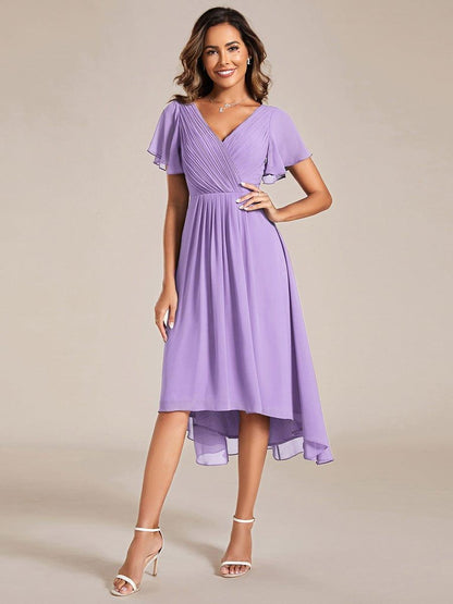 Model in the lilac chiffon dress, front view, hand on hip, with white strappy heels and a layered necklace. 100