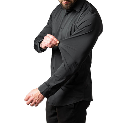Side view of a bearded man in a black long-sleeved shirt pinching and stretching the sleeve fabric to show its elasticity. 1