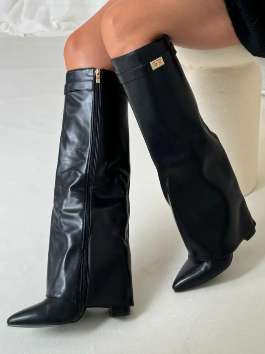 Black faux leather fold-over knee boots worn by a seated model, with side zip and gold turn-lock strap. 10