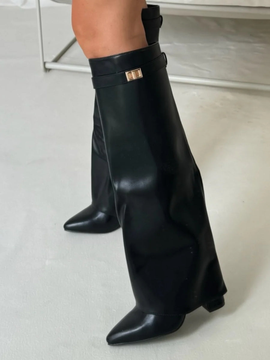 Black faux leather fold-over knee boots worn by a model, showing the glossy finish and gold turn-lock strap. 11