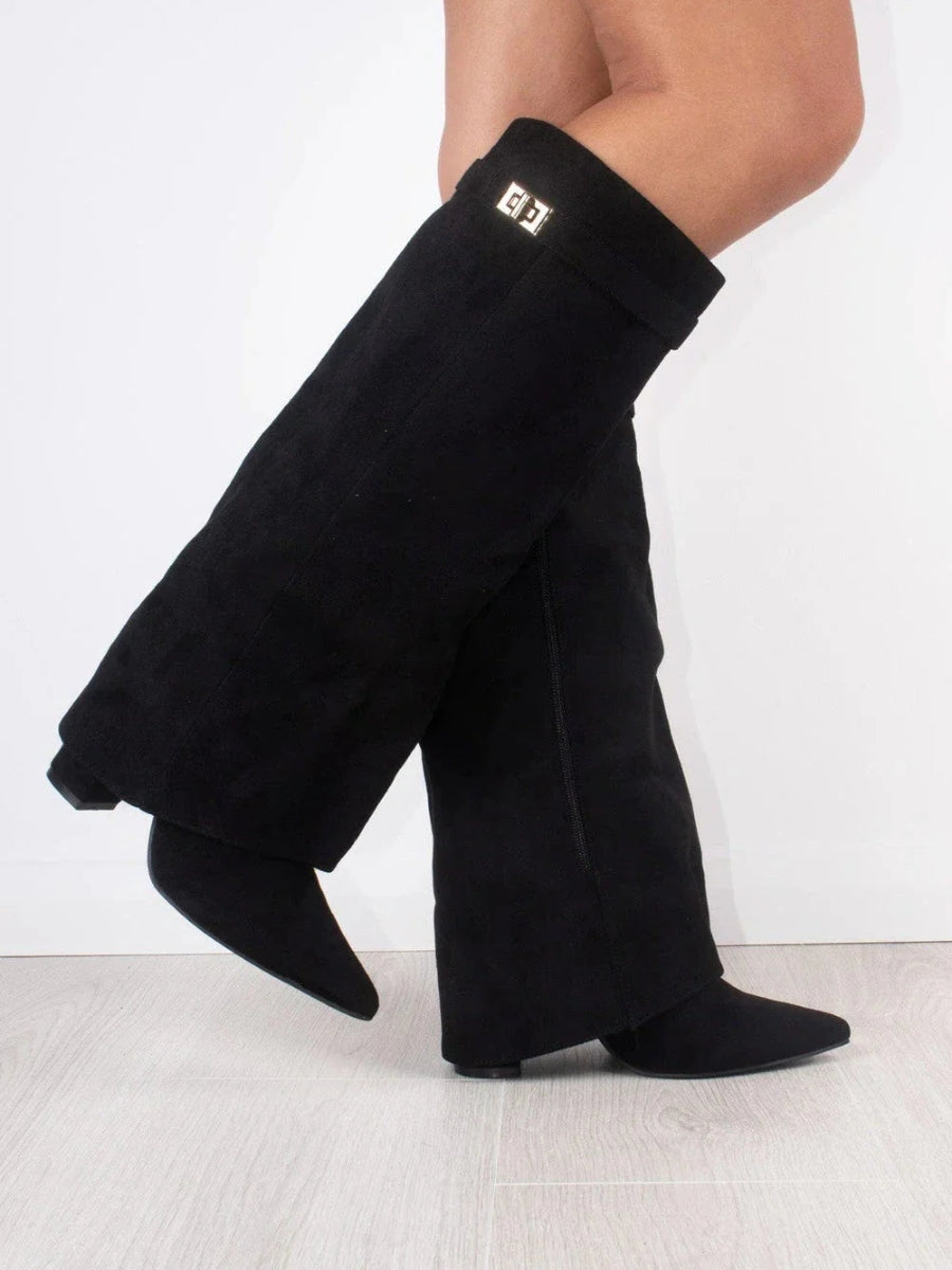 Black suede-look fold-over boots worn by a model mid-step, showing the gold turn-lock strap and a side zip. 2