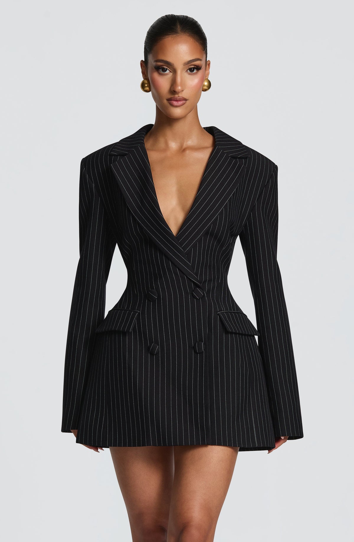 Front view of a black pinstripe blazer dress with fine white stripes, double-breasted covered buttons and a plunging neckline. 20