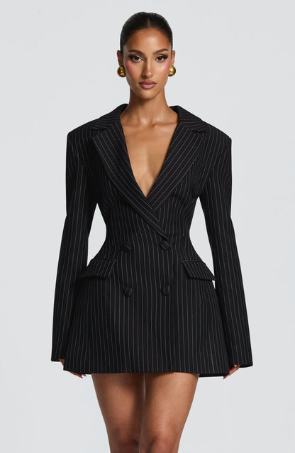 Front view of a black pinstripe blazer dress with fine white stripes, double-breasted covered buttons and a plunging neckline. 20