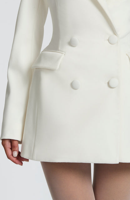 Detail of the ivory blazer dress below the waist, showing a flap pocket, covered buttons and the flared skirt. 16