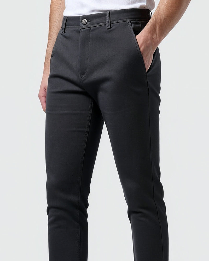 Close-up of dark charcoal chinos at the waist and hip, showing the button, belt loops and a hand in the side pocket. 10