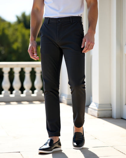 Dark charcoal chinos with a white t-shirt and black leather loafers, worn on a sunny terrace with white balustrade. 7