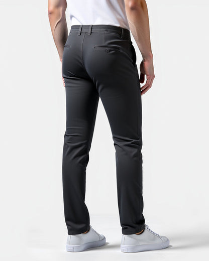 Back view of dark charcoal chinos on a model, showing buttoned back pockets and belt loops, with white trainers. 8