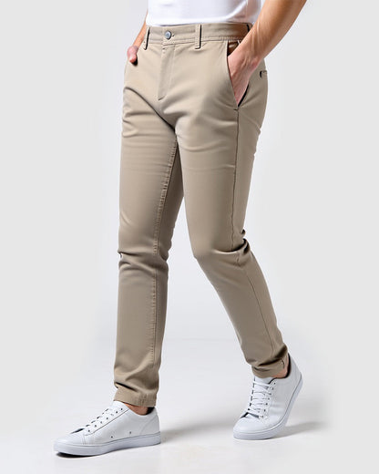 Beige chinos worn by a model with a white t-shirt and white trainers, angled side view with hands in pockets. 14