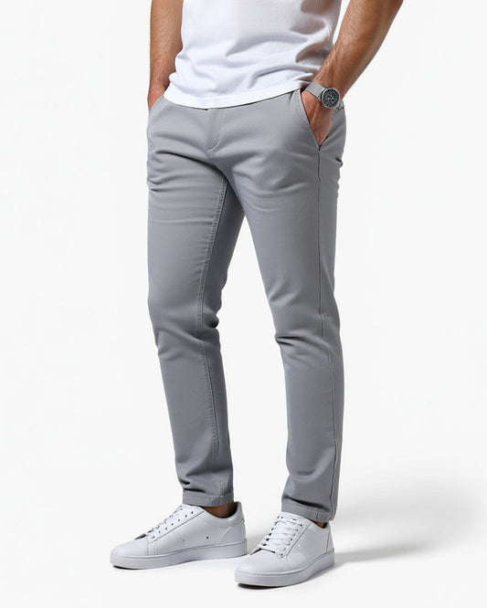 Light grey slim chinos worn by a model with a white t-shirt, white trainers and a watch, angled front view. 1