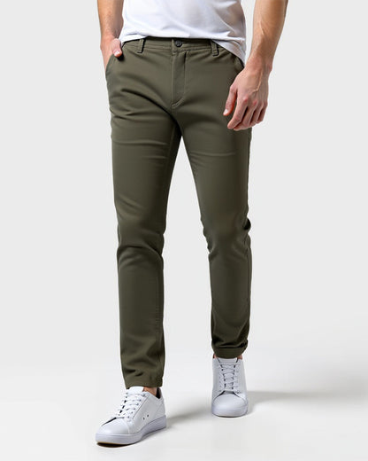 Olive green chinos worn by a model with a white t-shirt and white trainers, front view with one hand in the pocket. 13