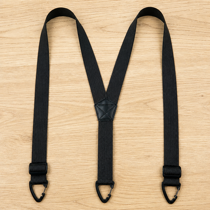Black Y-back suspenders laid flat on a wooden surface, with the adjusters positioned low near the three black clips. 13