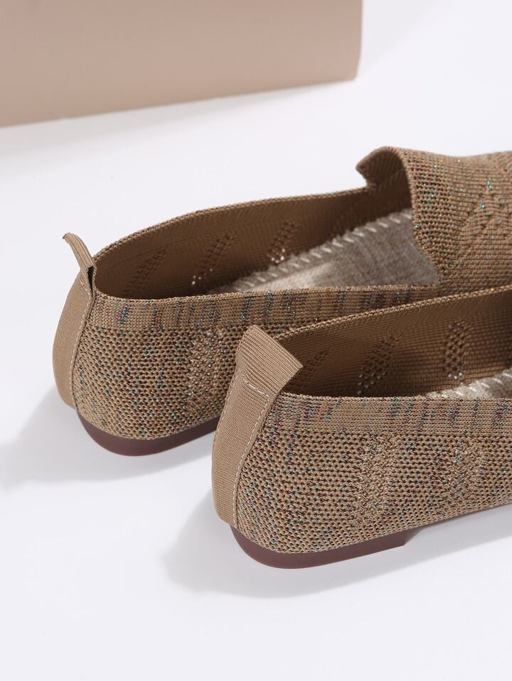 Close-up of the back of brown knit slip-ons, showing the heel pull tabs, flat sole and stitched footbed inside. 9