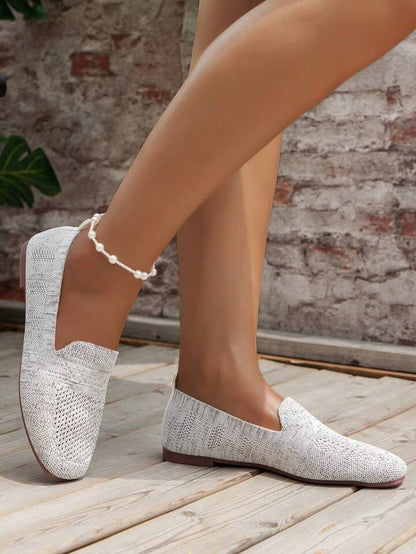 Light grey knit slip-ons with a flat sole, worn with a pearl anklet in front of a brick wall. 14