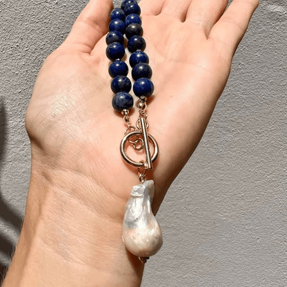 Necklace held across a palm against a grey wall, with the toggle clasp and pearl pendant visible 3