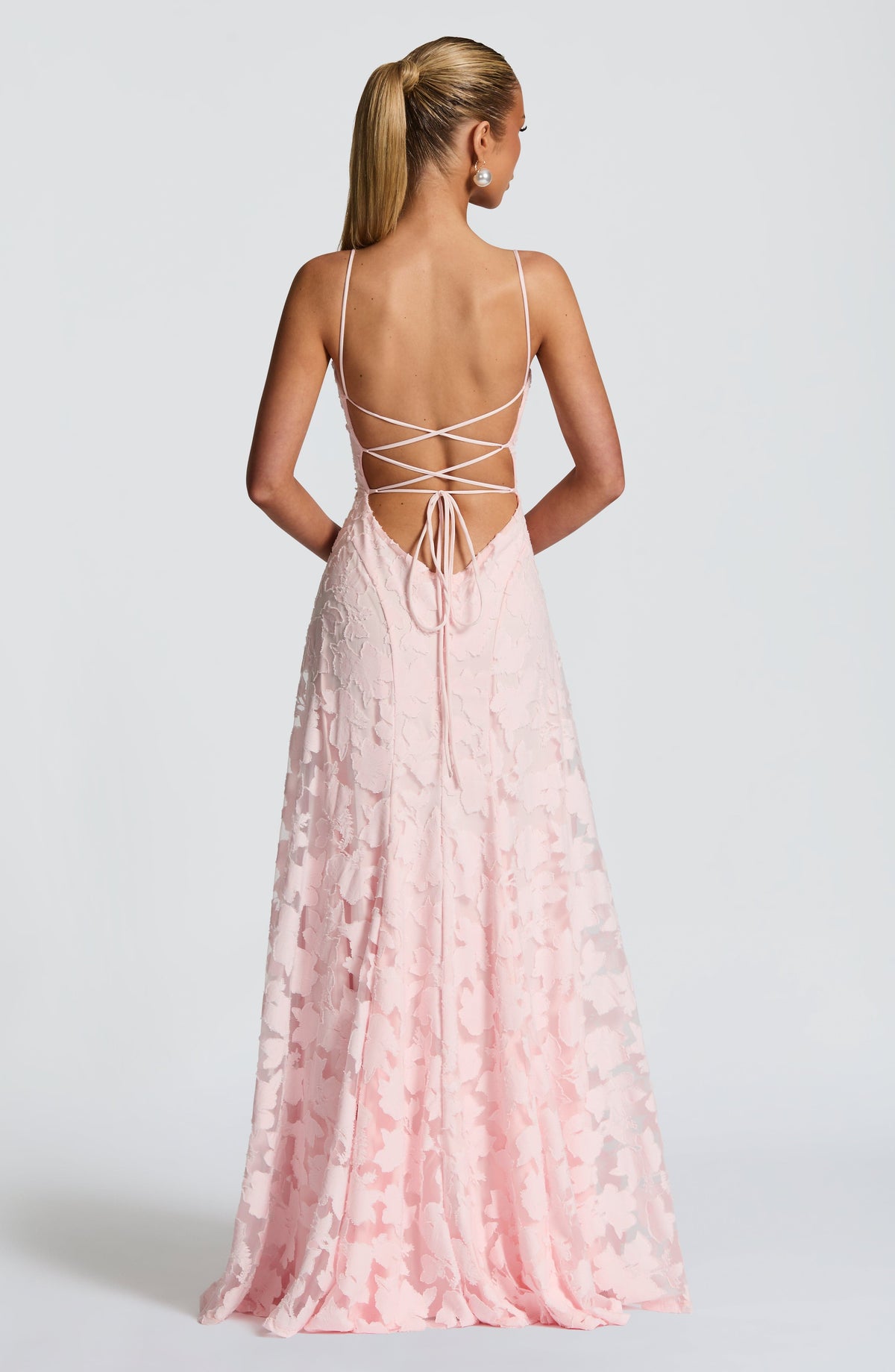 Back view of the pale pink floral maxi dress, showing the open back with criss-cross lace-up ties and flowing skirt. 2