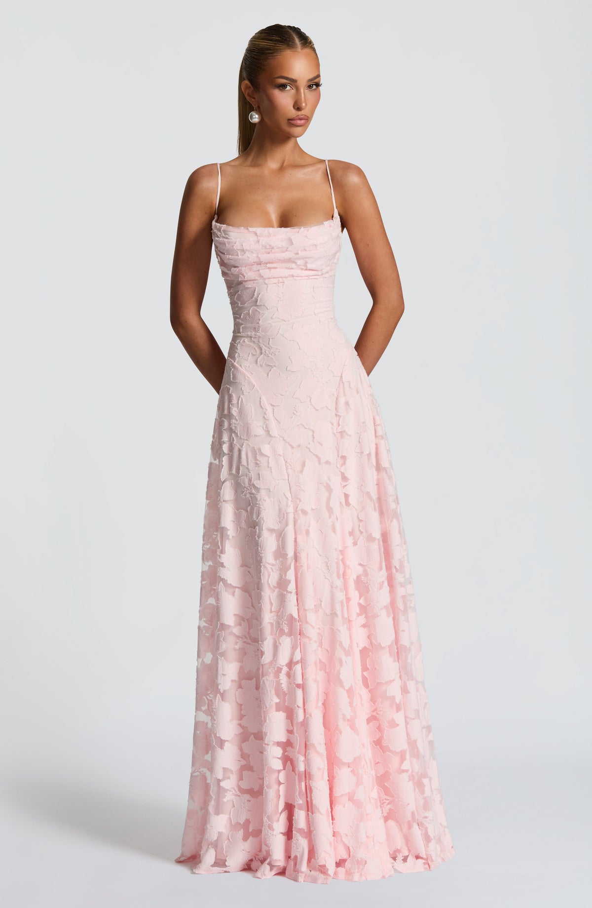 Model facing the camera in a pale pink floral jacquard maxi dress with a draped cowl neckline and thin straps. 1