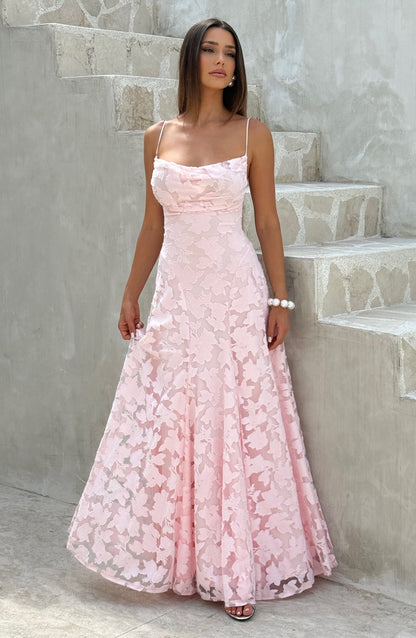 Brunette model in the pale pink floral maxi dress standing beside stone steps, holding the skirt slightly. 7