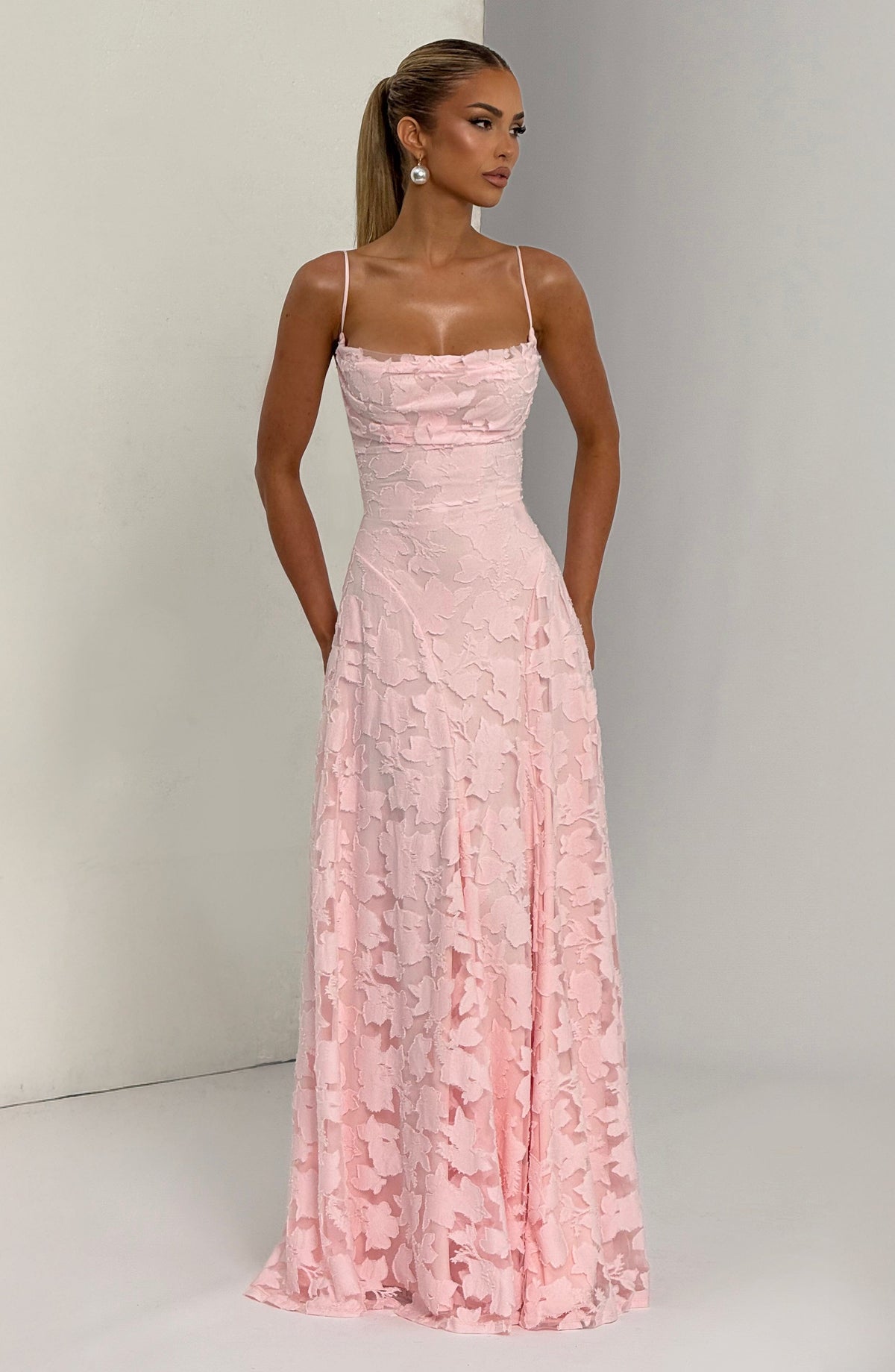 Model in the pale pink floral maxi dress looking to the side, with pearl earrings and a slicked-back ponytail. 5