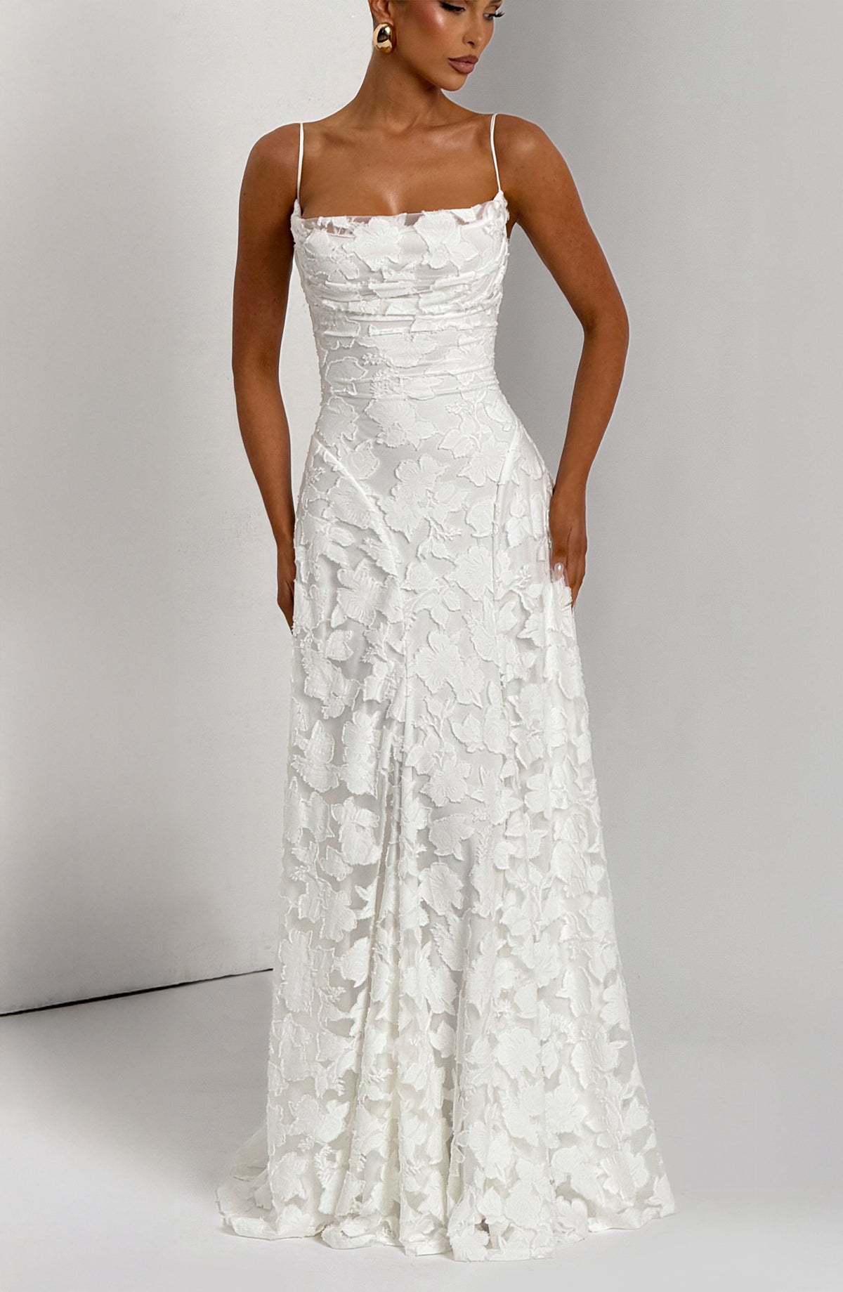 Front view of the white floral maxi dress against a grey studio wall, with fitted bodice and long fluid skirt. 14