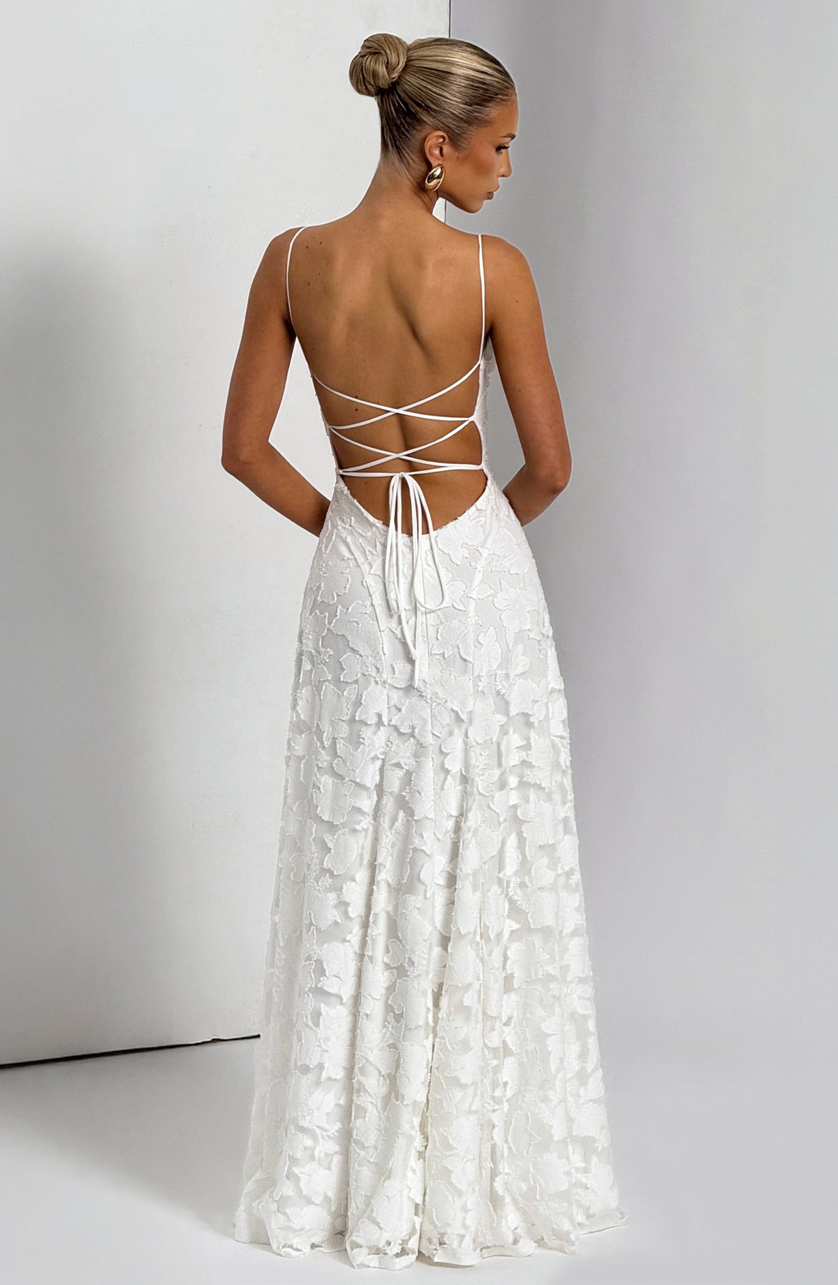 Back view of the white maxi dress against a grey wall, showing the criss-cross lace-up back and long flowing skirt. 15