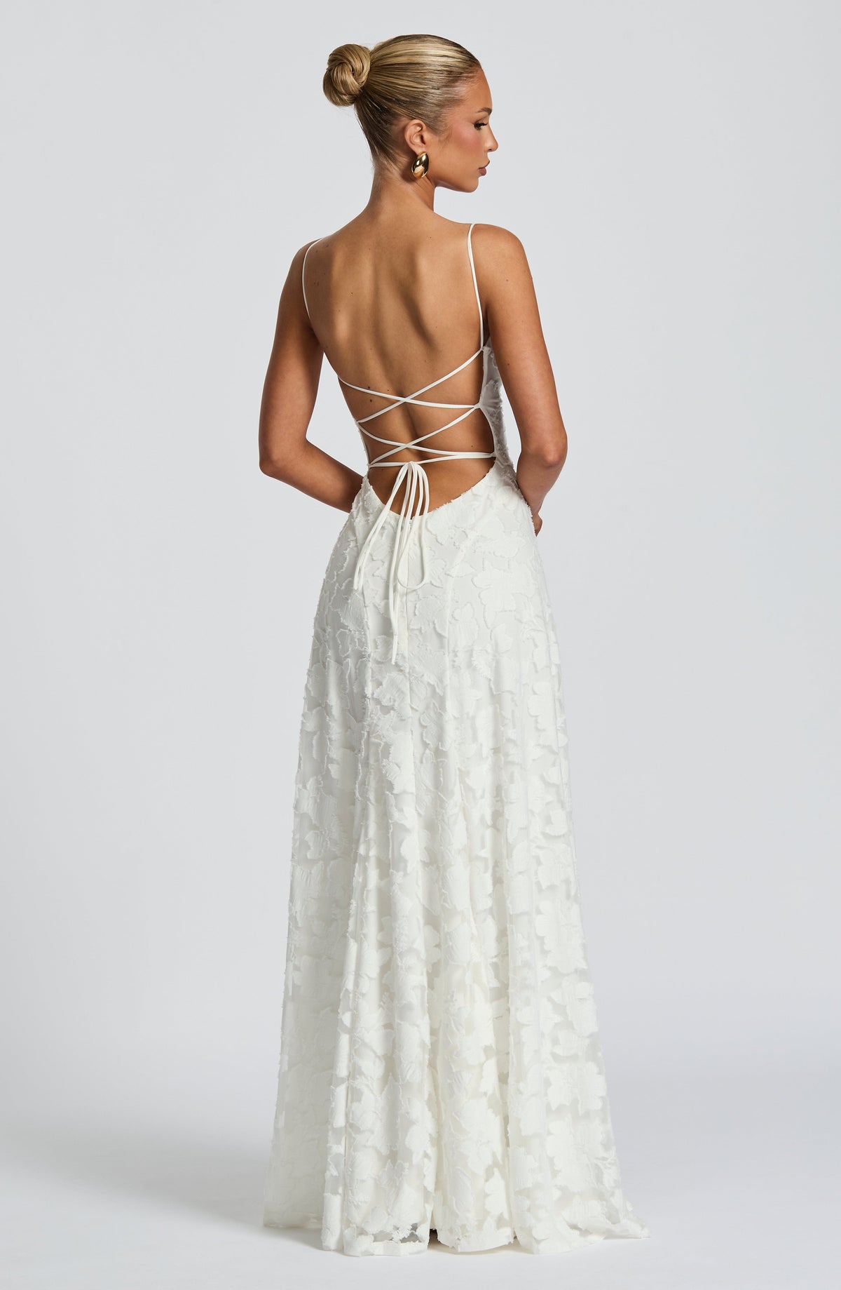 Back view of the white floral maxi dress, showing the open back with criss-cross ties and the model's hair in a bun. 11
