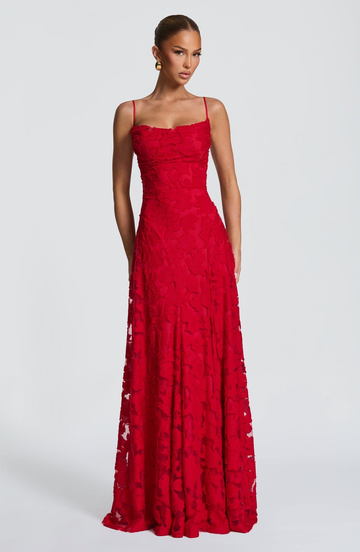 Front view of the dress in red, worn by a model, with a cowl neckline and floral textured long skirt. 24