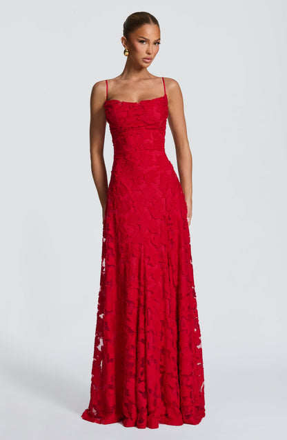 Front view of the dress in red, worn by a model, with a cowl neckline and floral textured long skirt. 24