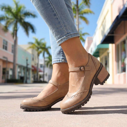 Low-angle view of beige shoes worn on a sunny street, showing the perforated toe, ankle strap and block heel 9