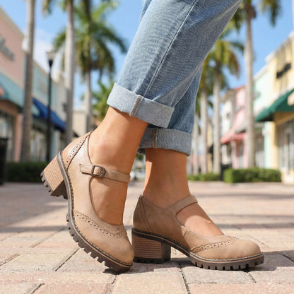 Beige shoes worn on a palm-lined street with cuffed jeans, side view showing buckle strap and wooden-effect heel 6