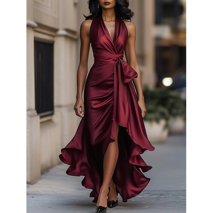 Front view of the satin halter dress in burgundy, worn by a model on a city pavement, showing waist bow and ruffles. 2