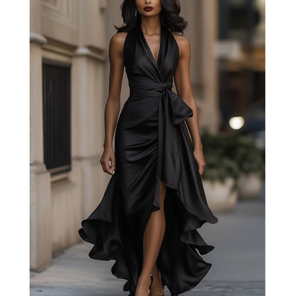 Front view of the halter dress in black satin on a model walking, with draped bodice, waist tie and ruffled slit hem. 7