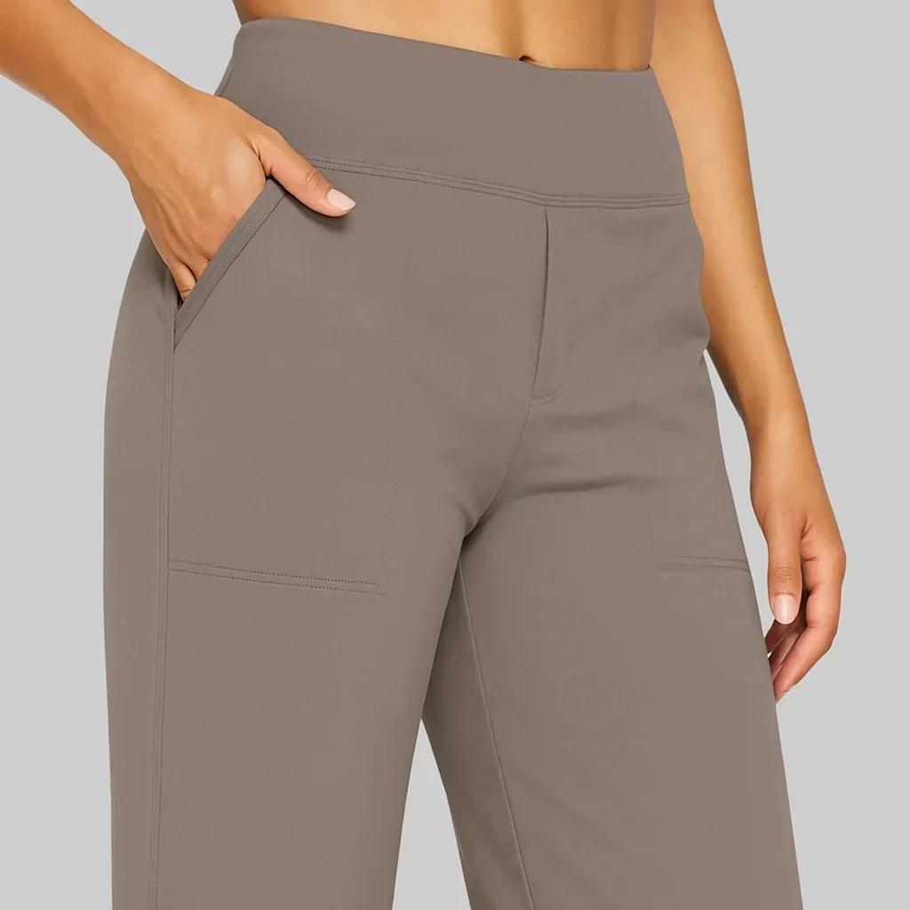Close-up of the wide waistband, side pocket and stitched front patch pockets on the taupe trousers, with a hand in the pocket. 3