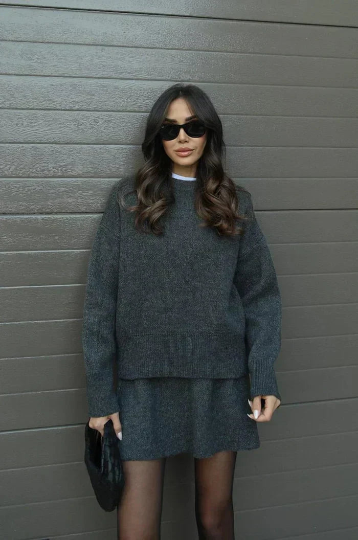 Model in the charcoal grey set holding a black woven clutch, facing the camera 11