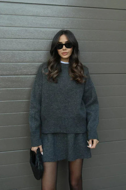 Model in the charcoal grey set holding a black woven clutch, facing the camera 11