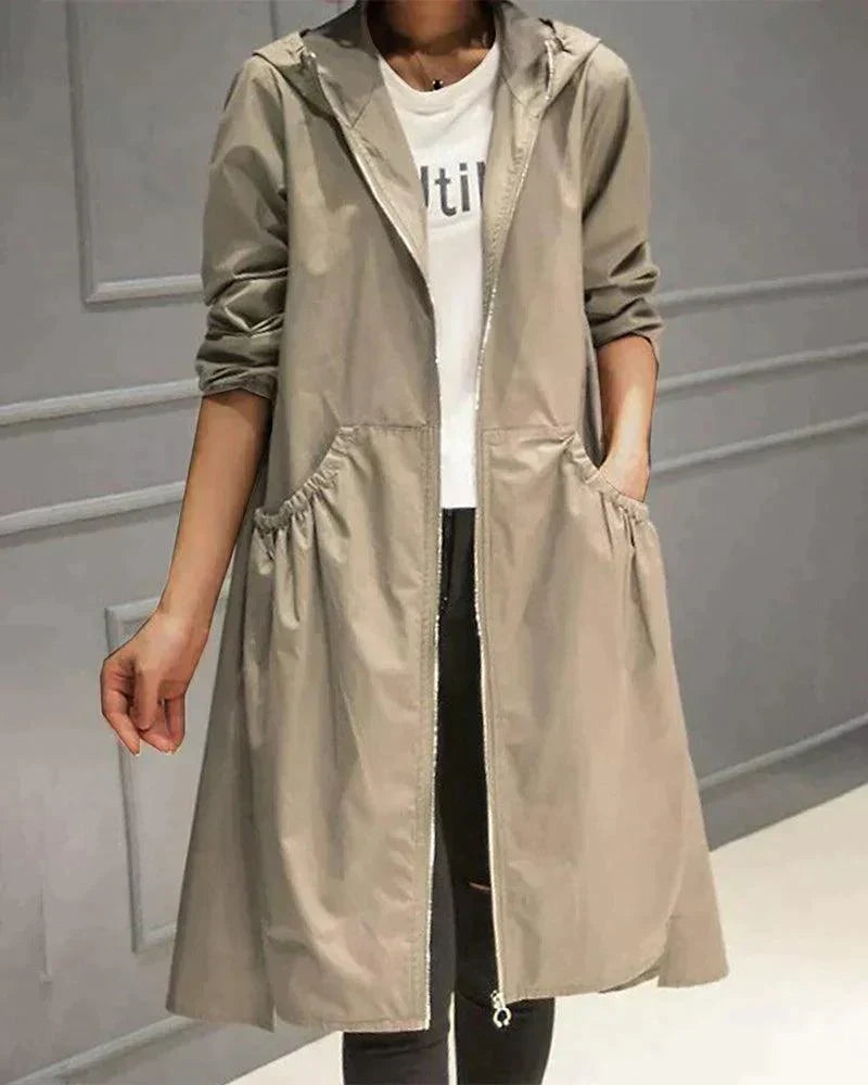 Model wearing the open-fronted, zip-up hooded raincoat in light khaki, hand in a gathered side pocket 1