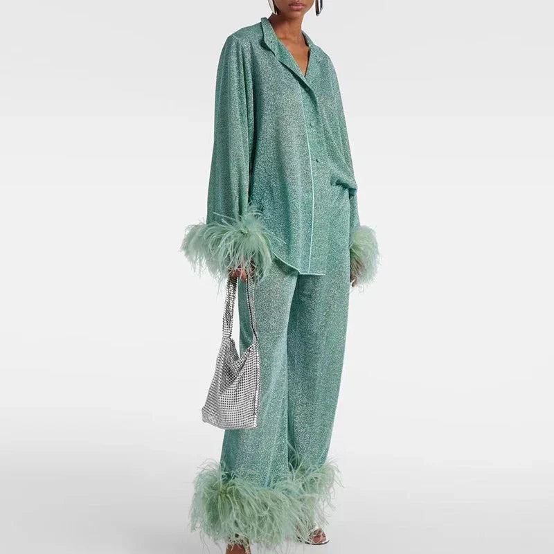 Model in the sea-green glitter set with notched collar, piped shirt and feather-trimmed cuffs and wide trousers, carrying a silver mesh bag. 2