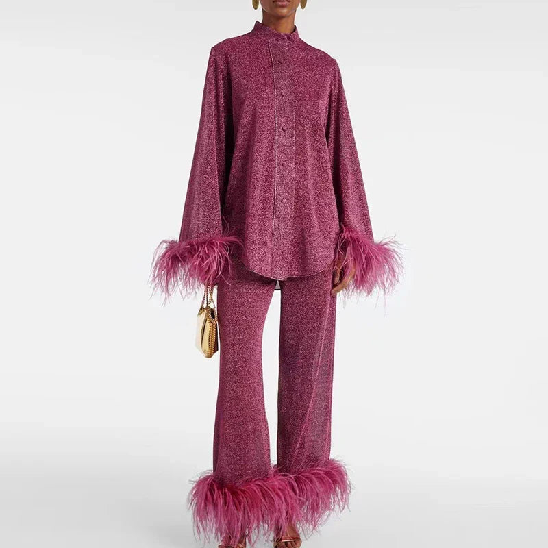 Model in the berry-pink glitter set with high collar, buttoned shirt and feather-trimmed cuffs and trouser hems, holding a small gold clutch. 1