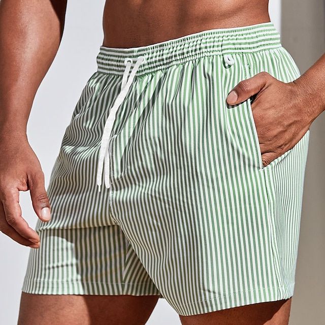 Model wearing light green and white vertically striped swim shorts with a white drawstring, hand placed in the side pocket. 12