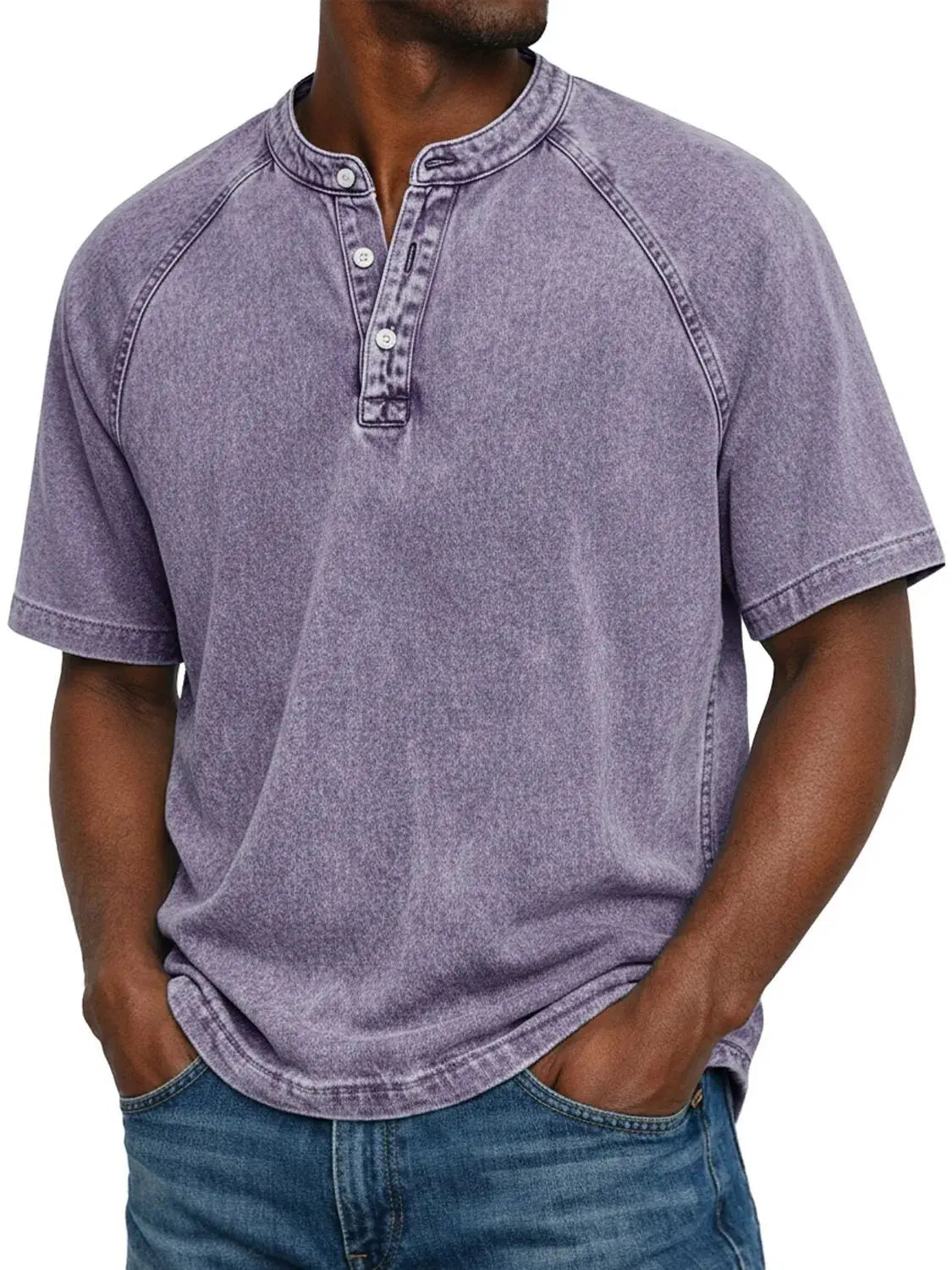 Man wearing the short-sleeved raglan Henley in washed lilac purple, three-button placket, hands in pockets of blue jeans. 1