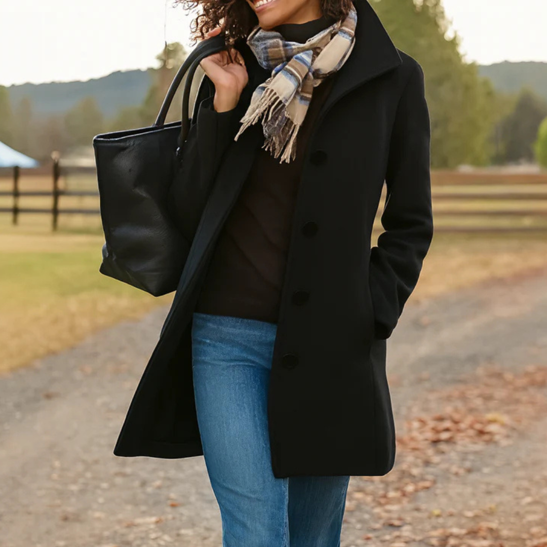 Black version of the coat worn open over a dark jumper and jeans, with a checked scarf and tote, outdoors. 3
