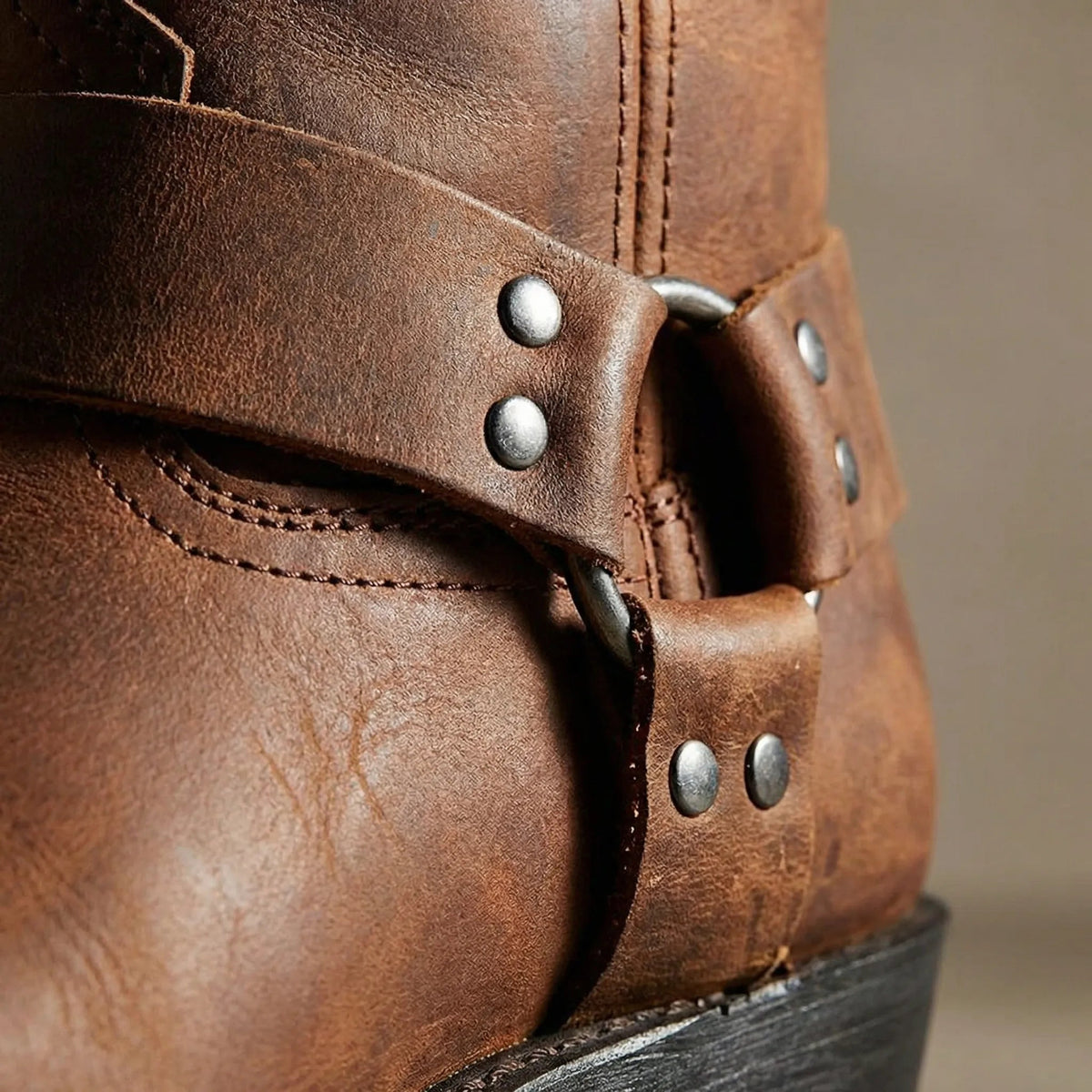 Close-up of the boot's harness strap, showing metal rivets, the ring and the grainy texture of the brown leather. 3