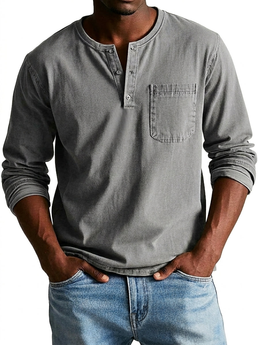 Model wearing the henley in mid grey, showing the button placket, chest pocket and pushed-up sleeves, with light blue jeans. 4