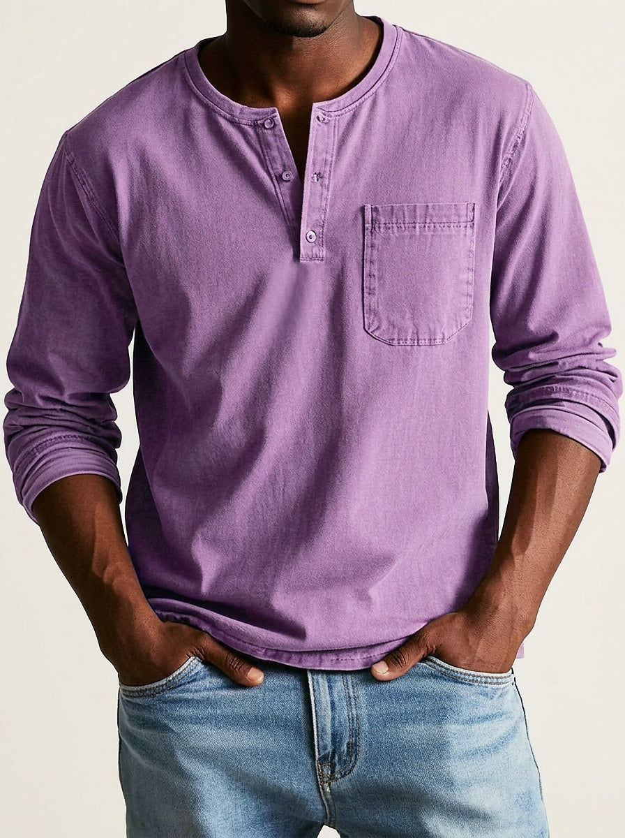Model wearing the henley in washed purple, front view with button placket and chest pocket, hands in light blue jeans. 8