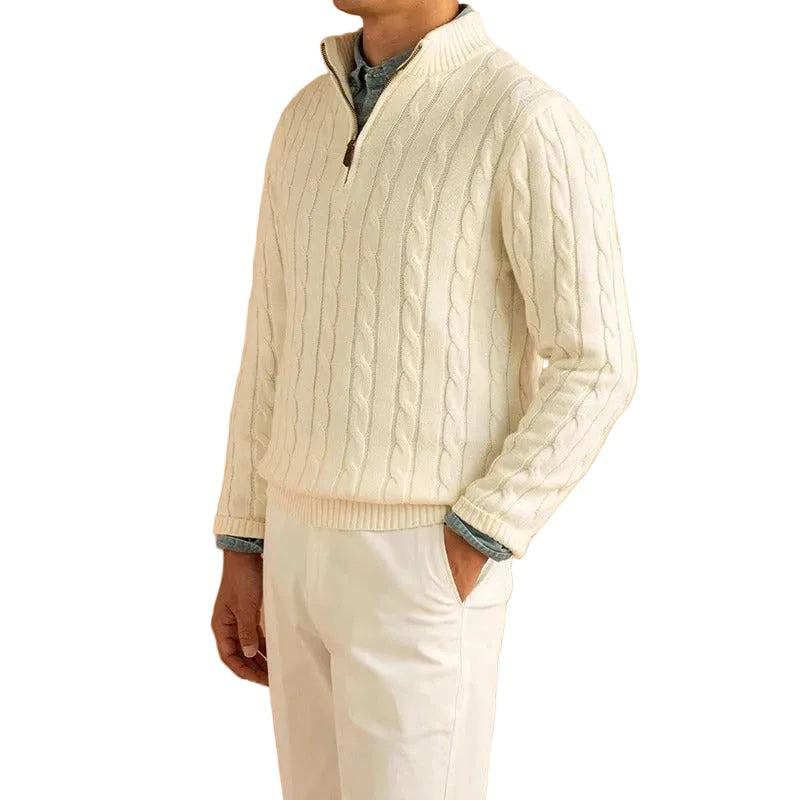 Man wearing the cream cable knit jumper with white trousers, hand in pocket, over a blue shirt 1