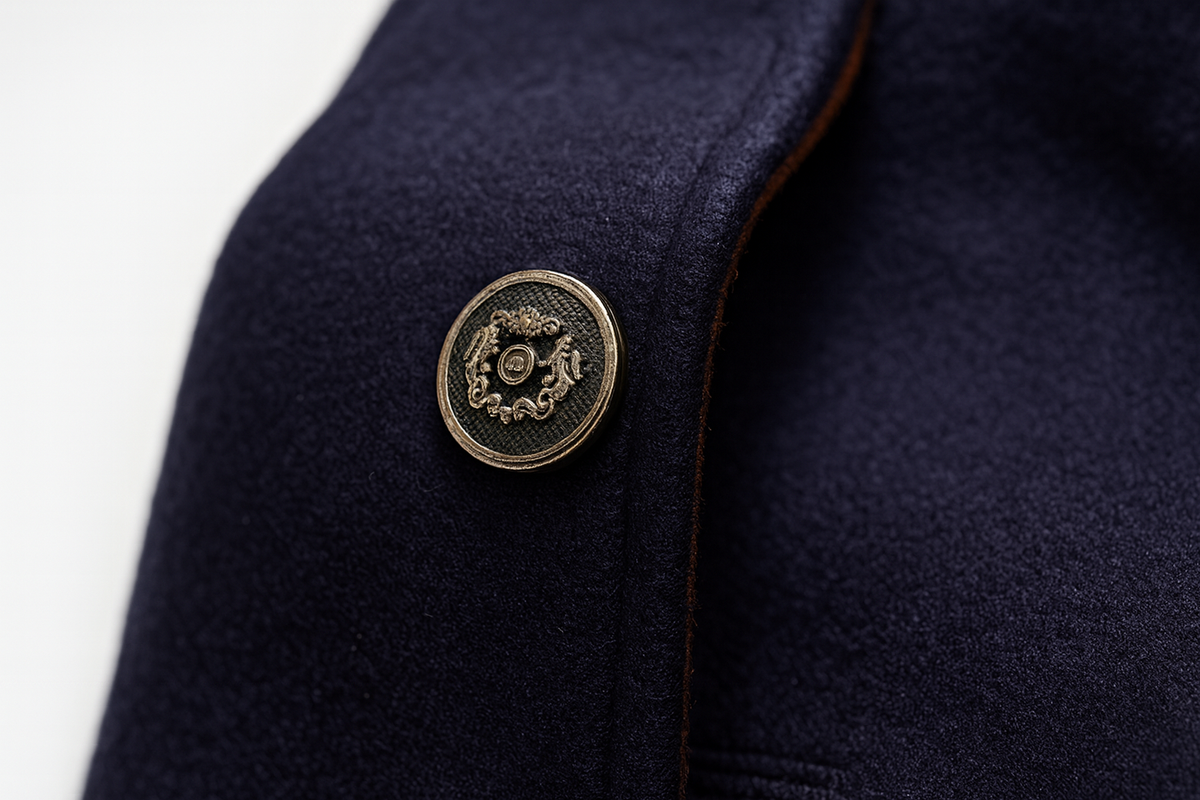 Close-up of an ornate metal button on navy wool fabric with a thin tan edge 10