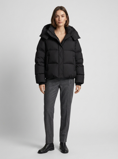 Model standing in the black puffer jacket with hood, worn with grey tailored trousers and black ankle boots 4